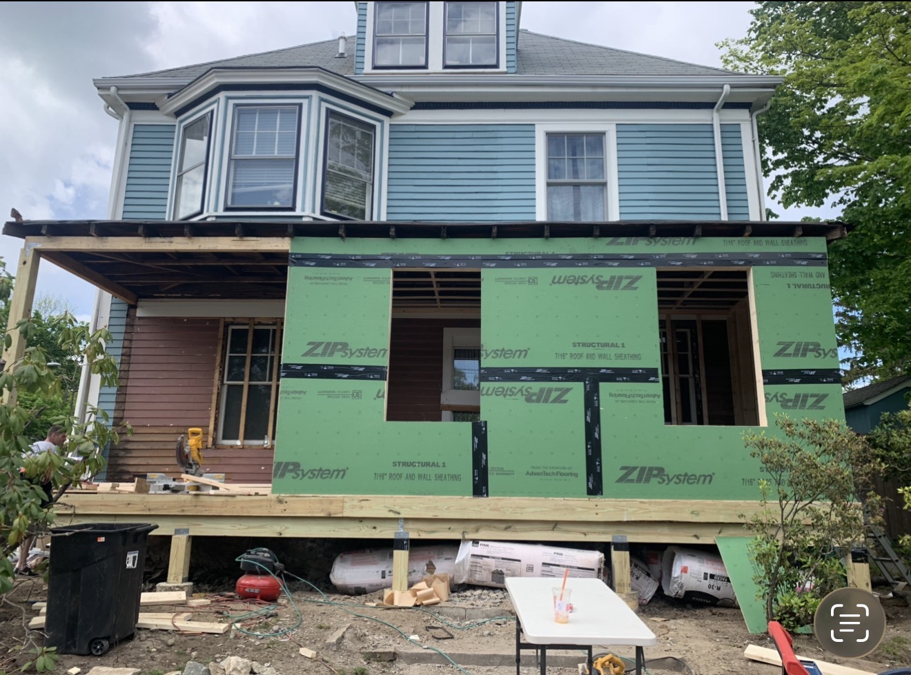 Two-story Victorian home addition mid-build with new pressure-treated deck framing and ZIP System sheathing wrapping the new bump-out