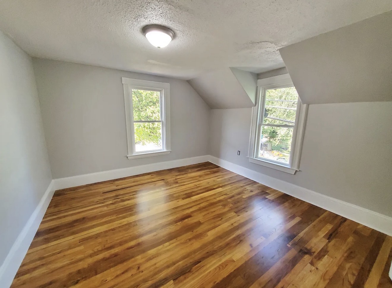 Refinished attic bedroom with restored hardwood floors, soft gray walls, white trim, and dormer windows