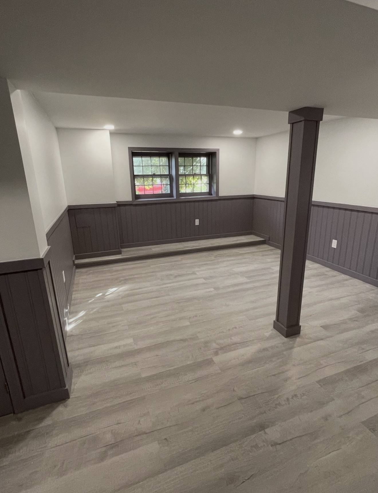 Finished basement with charcoal beadboard wainscoting, gray LVP flooring, and recessed lighting