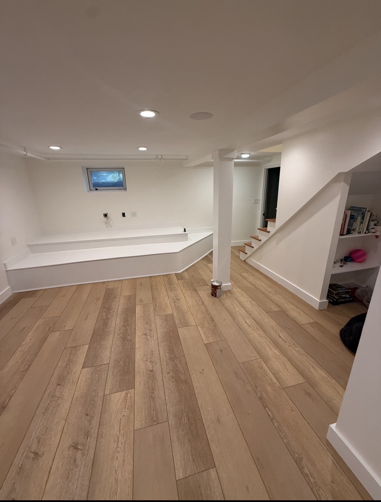 Finished basement playroom with bright white walls, built-in bookshelves under the stairs, and wide-plank LVP flooring