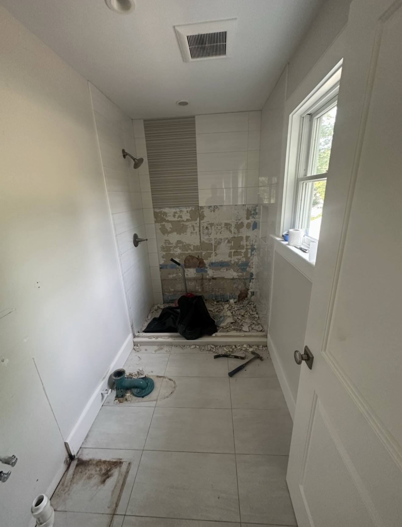 Bathroom remodel in progress — old shower tile demoed down to the substrate with debris and tools on the floor