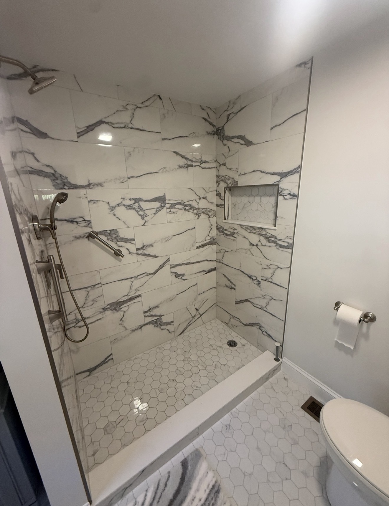 Custom walk-in shower with large-format marble-look porcelain tile, hex mosaic floor, and recessed niche
