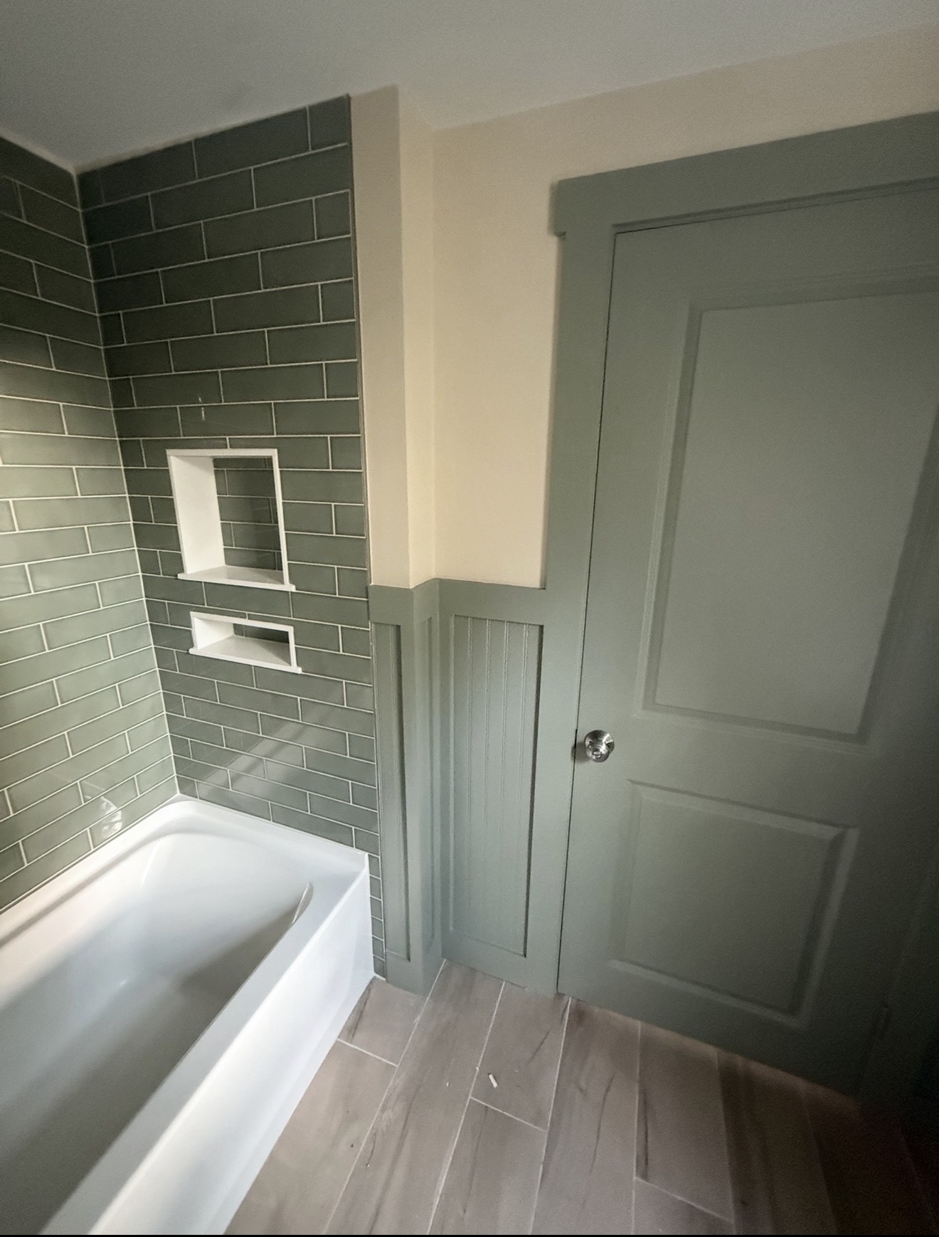 Bathroom remodel with sage green subway tile tub surround, matching board-and-batten wainscoting, and tile floor