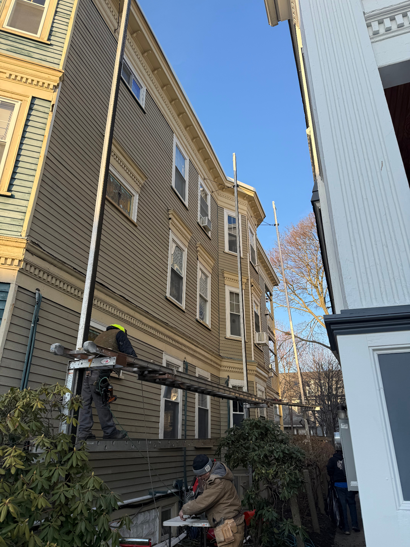 Dan's Painting & General Contracting crew on ladder jacks installing and prepping siding on a tall Victorian multi-family in Boston, MA