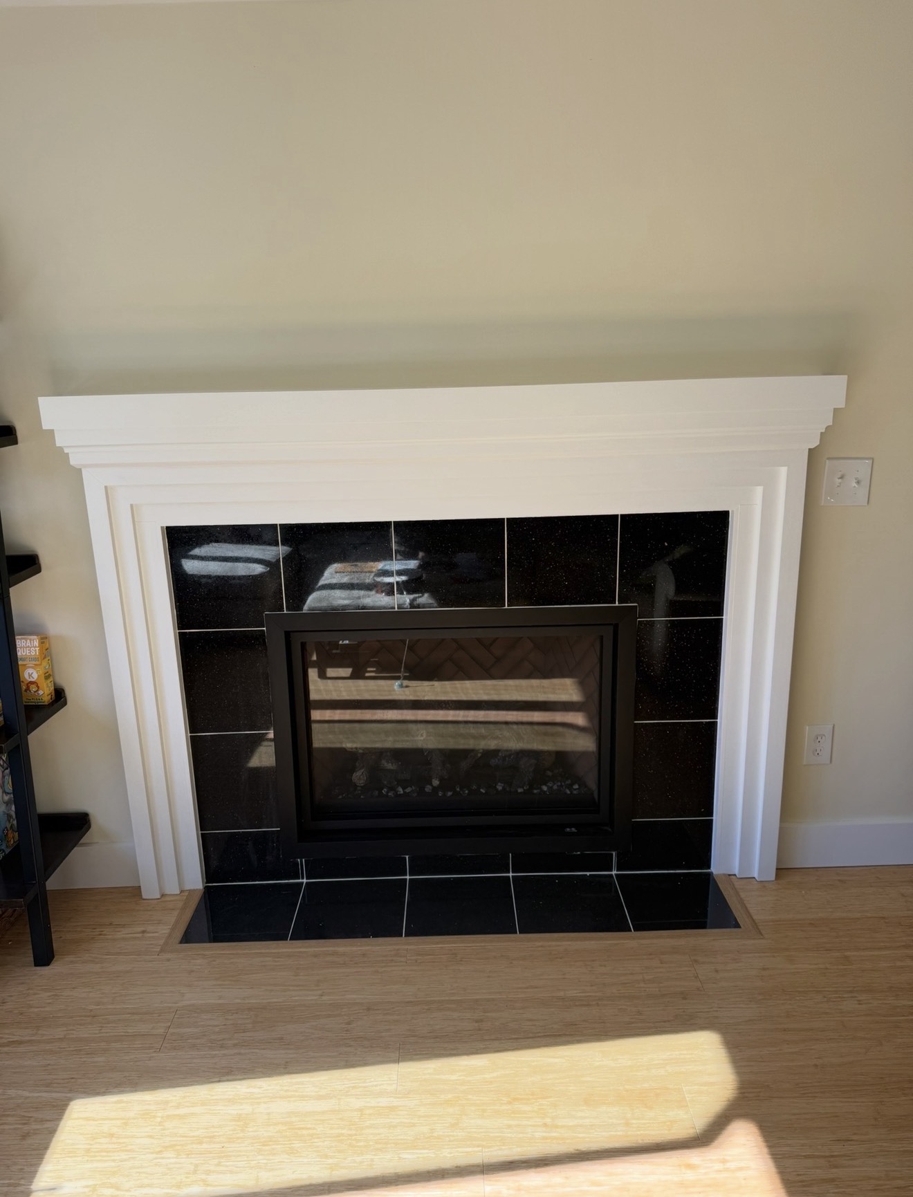Finished fireplace with polished black galaxy tile surround, custom white painted mantel, and crown molding details