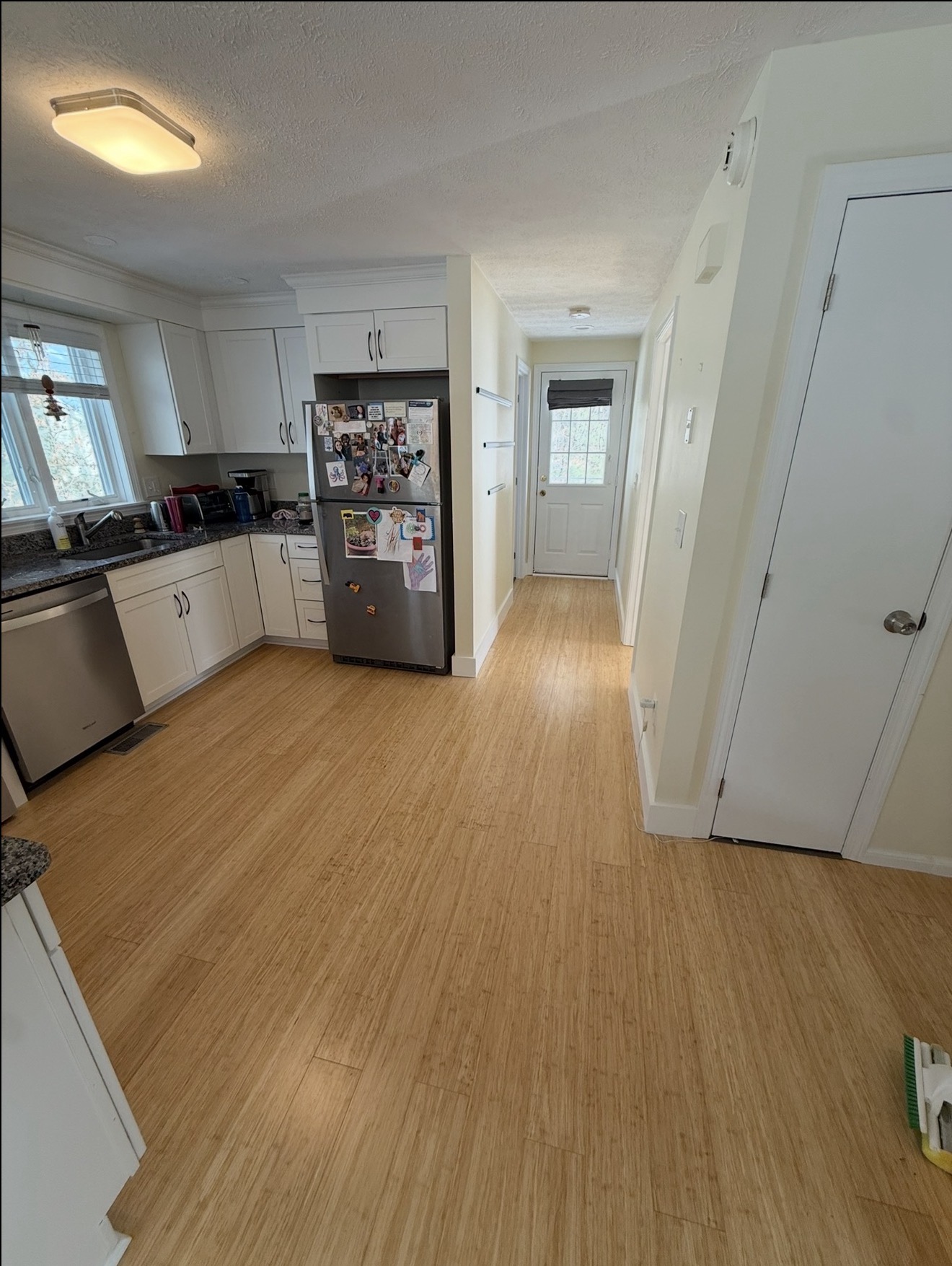 Galley kitchen with white shaker cabinets and worn bamboo flooring before installation of new wood-look LVP