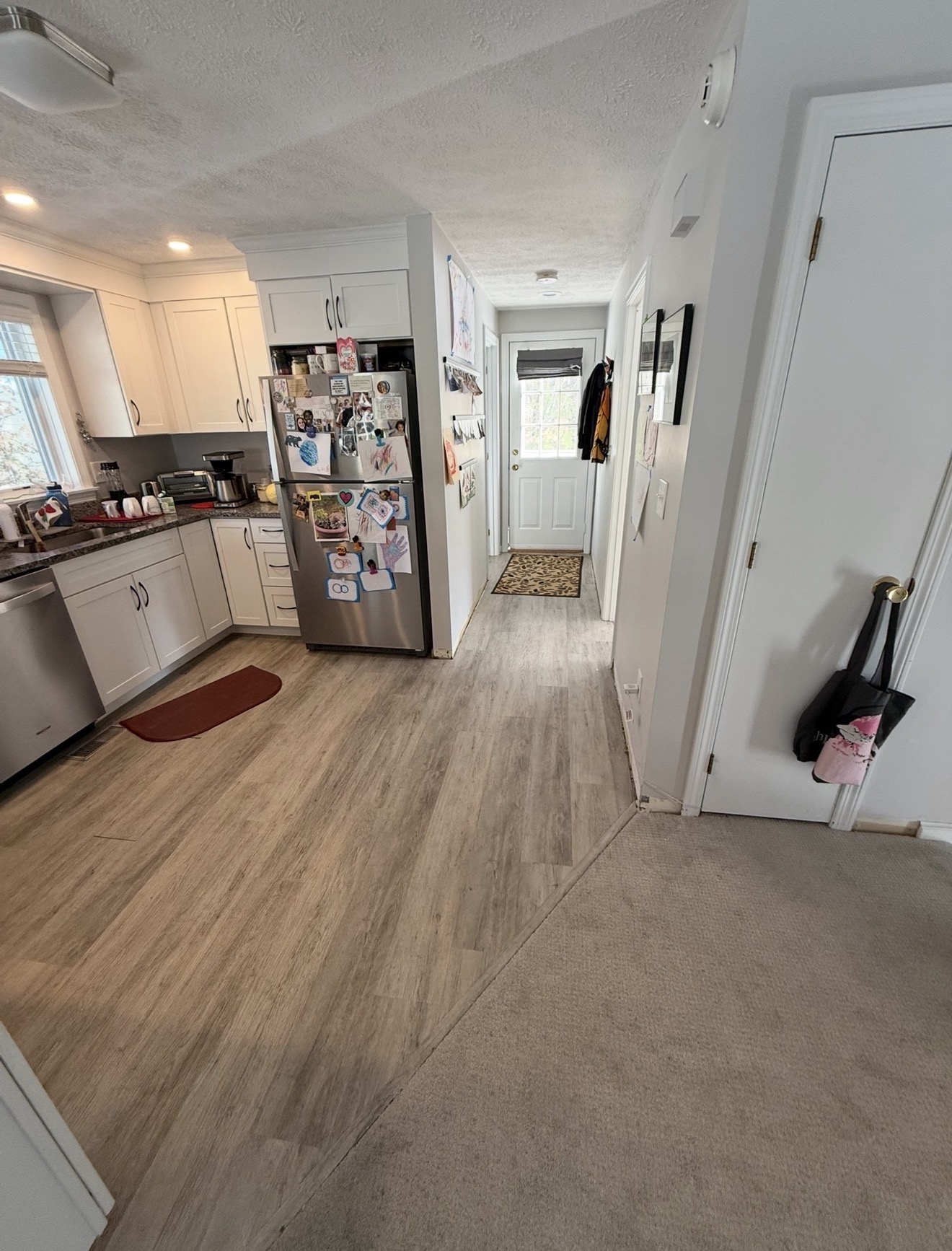 White shaker kitchen with stainless appliances and new wood-look LVP flooring transitioning to hallway
