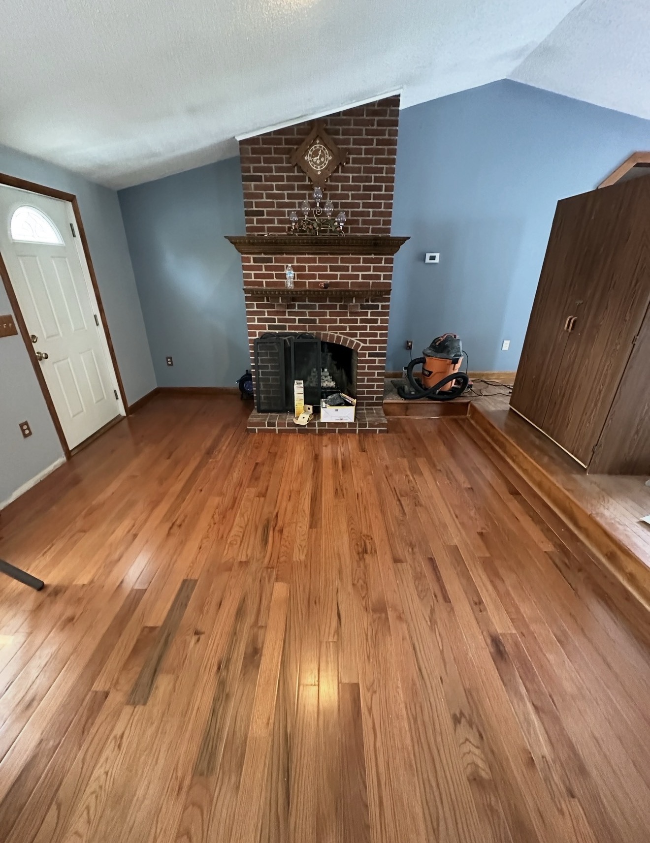 Living room with refinished red oak hardwood floors and original brick fireplace before repainting