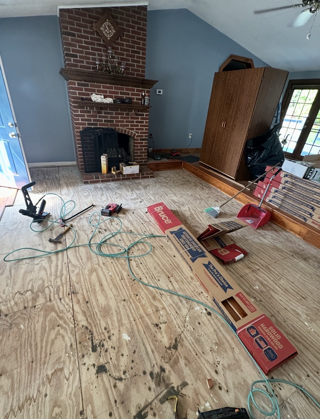 Living room with brick fireplace stripped down to plywood subfloor with new Bruce solid hardwood ready for installation