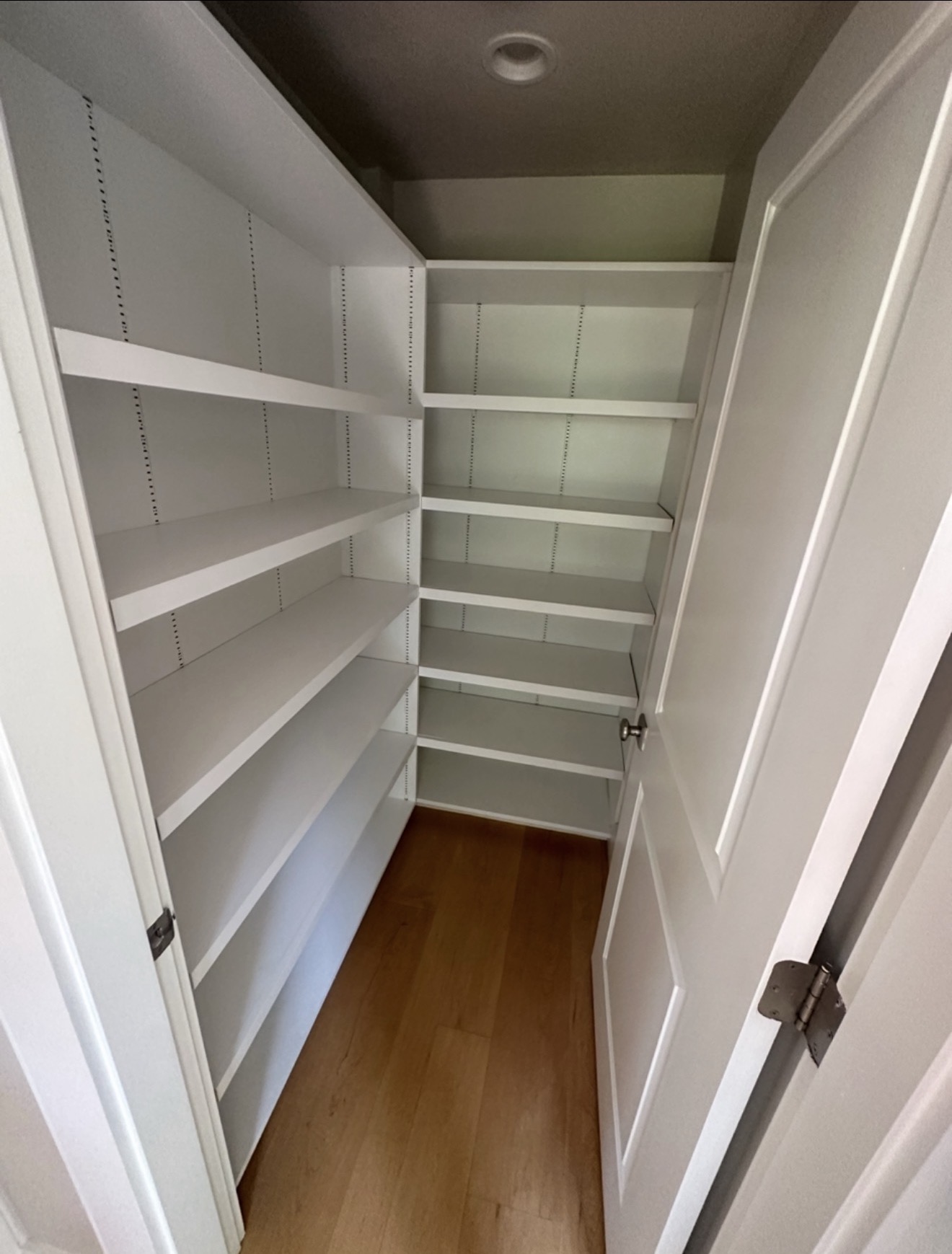 Custom-built walk-in pantry with adjustable white shelves, wraparound storage, and oak hardwood floor