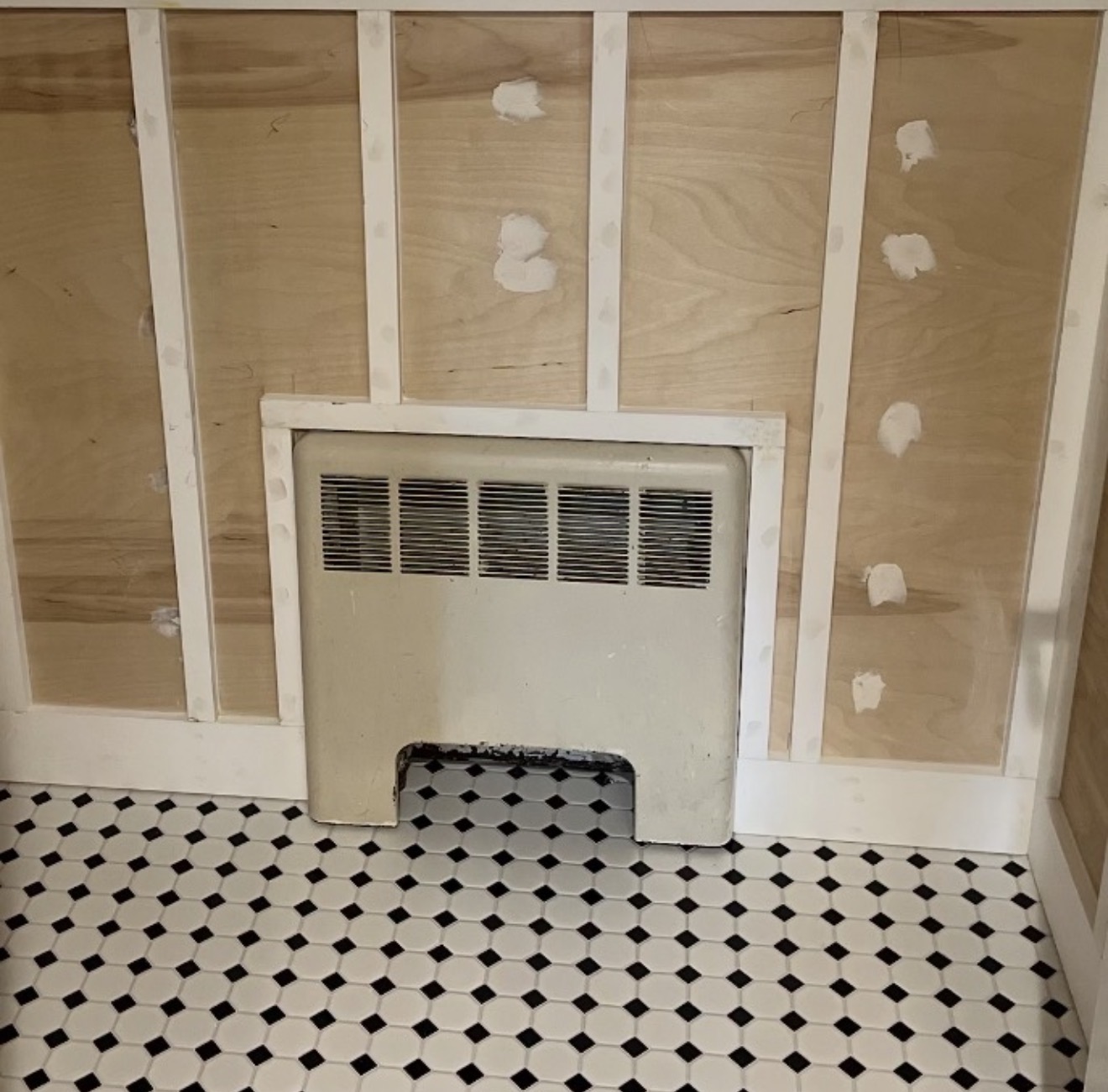 Powder room mid-renovation with newly installed beadboard wainscoting in primer, spackled nail holes, and classic black-and-white octagon tile floor