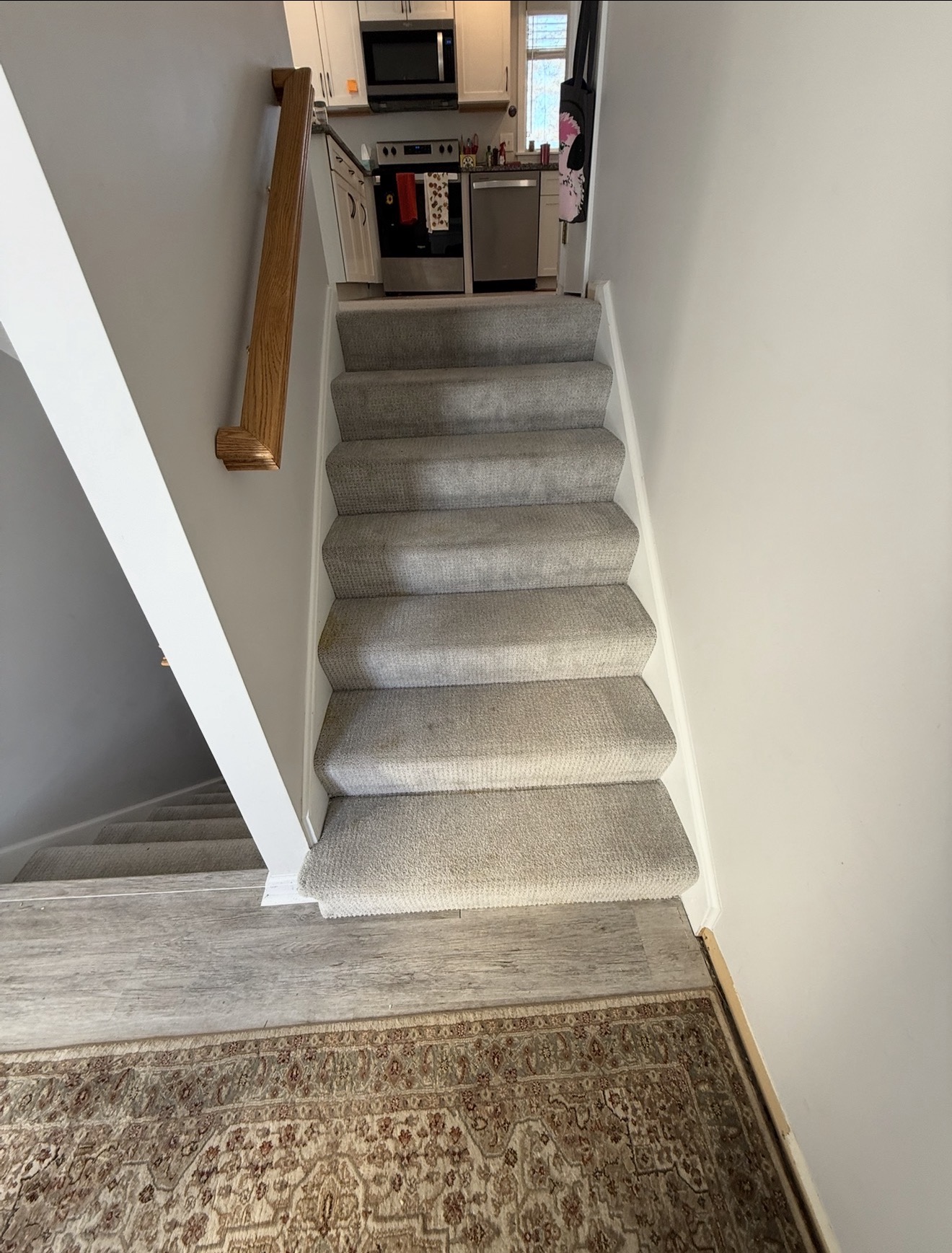 Tired beige carpeted staircase with worn treads leading up to a kitchen — before refinishing