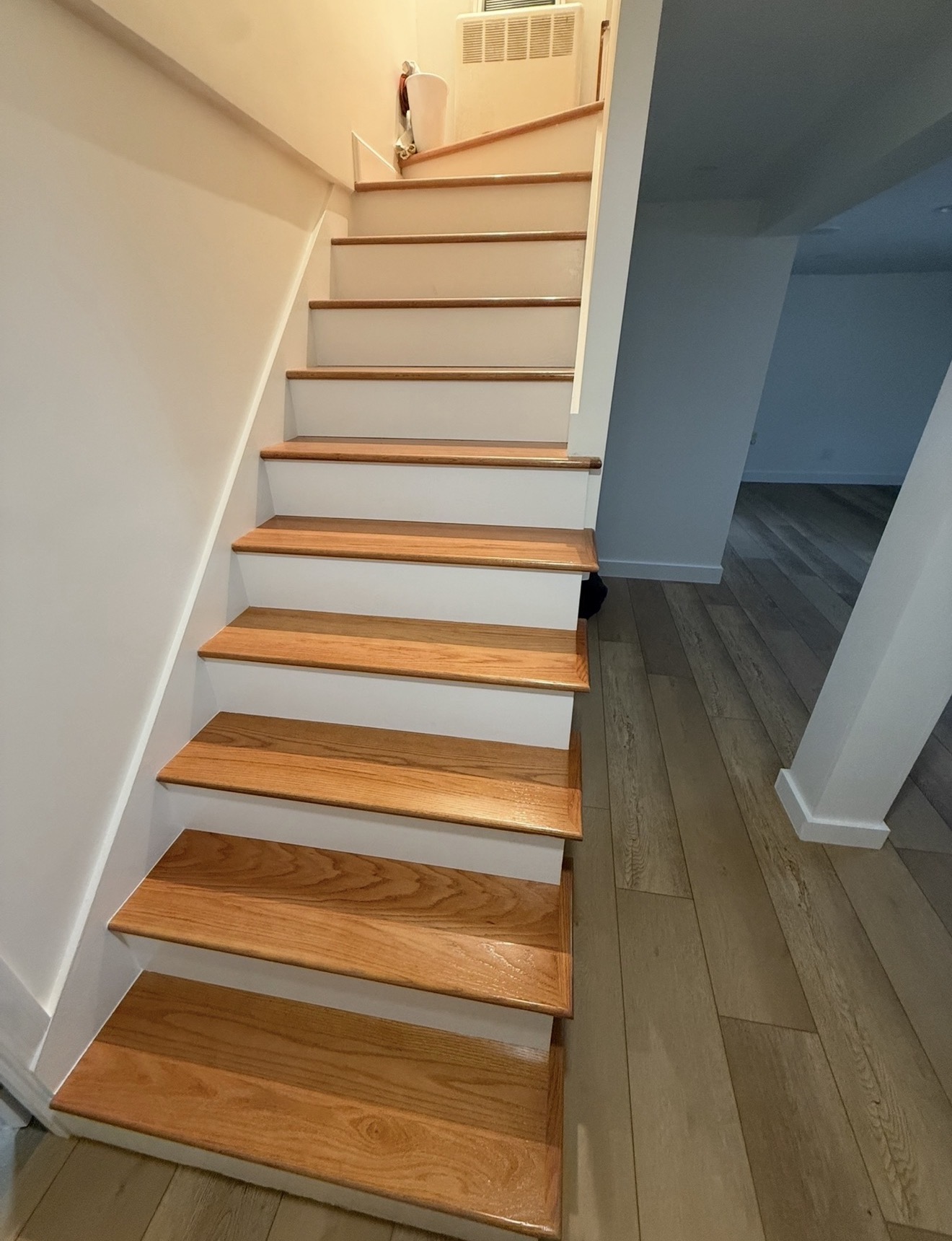 Finished red oak staircase with crisp white risers leading down to a finished basement with LVP flooring