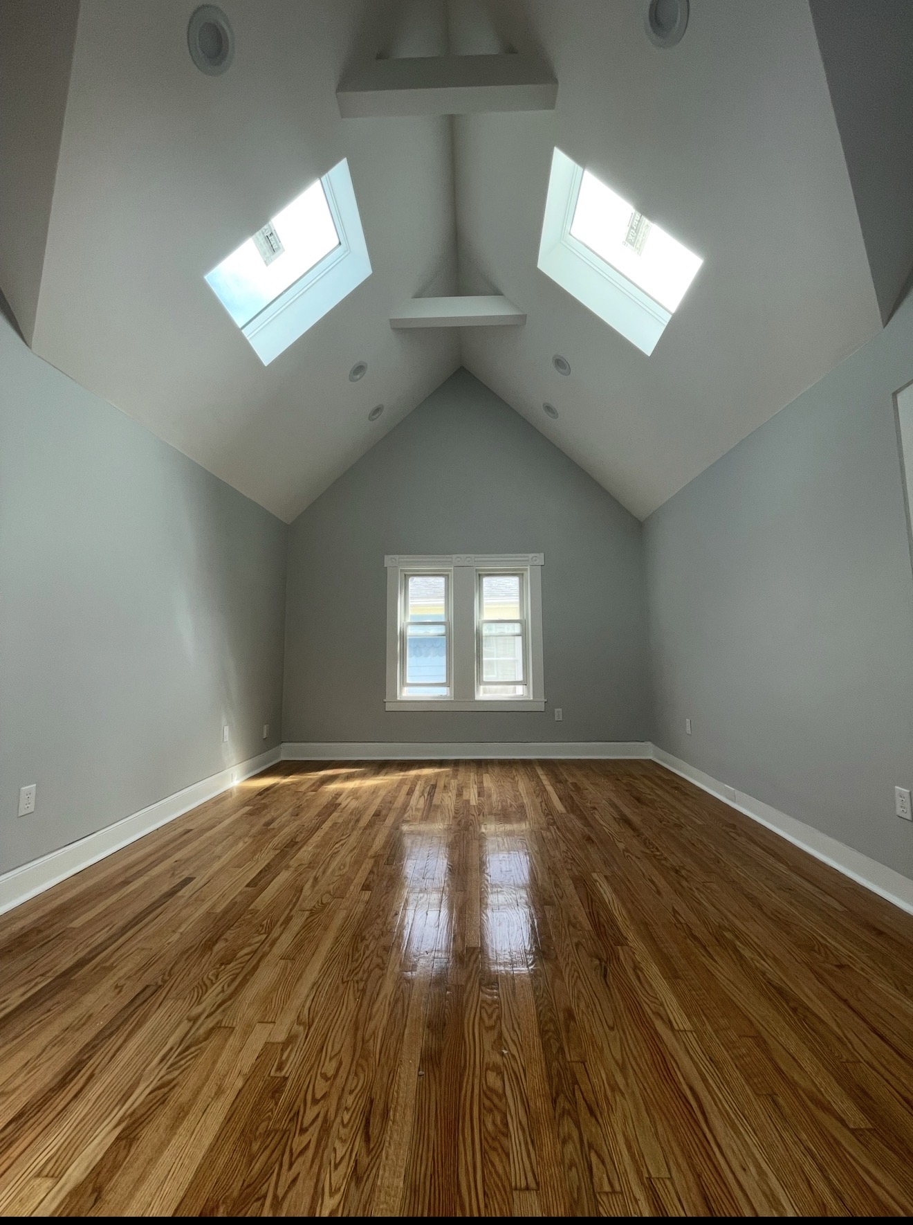 Vaulted-ceiling bedroom with twin skylights, refinished red oak hardwood floors, soft warm gray walls, and crisp white trim